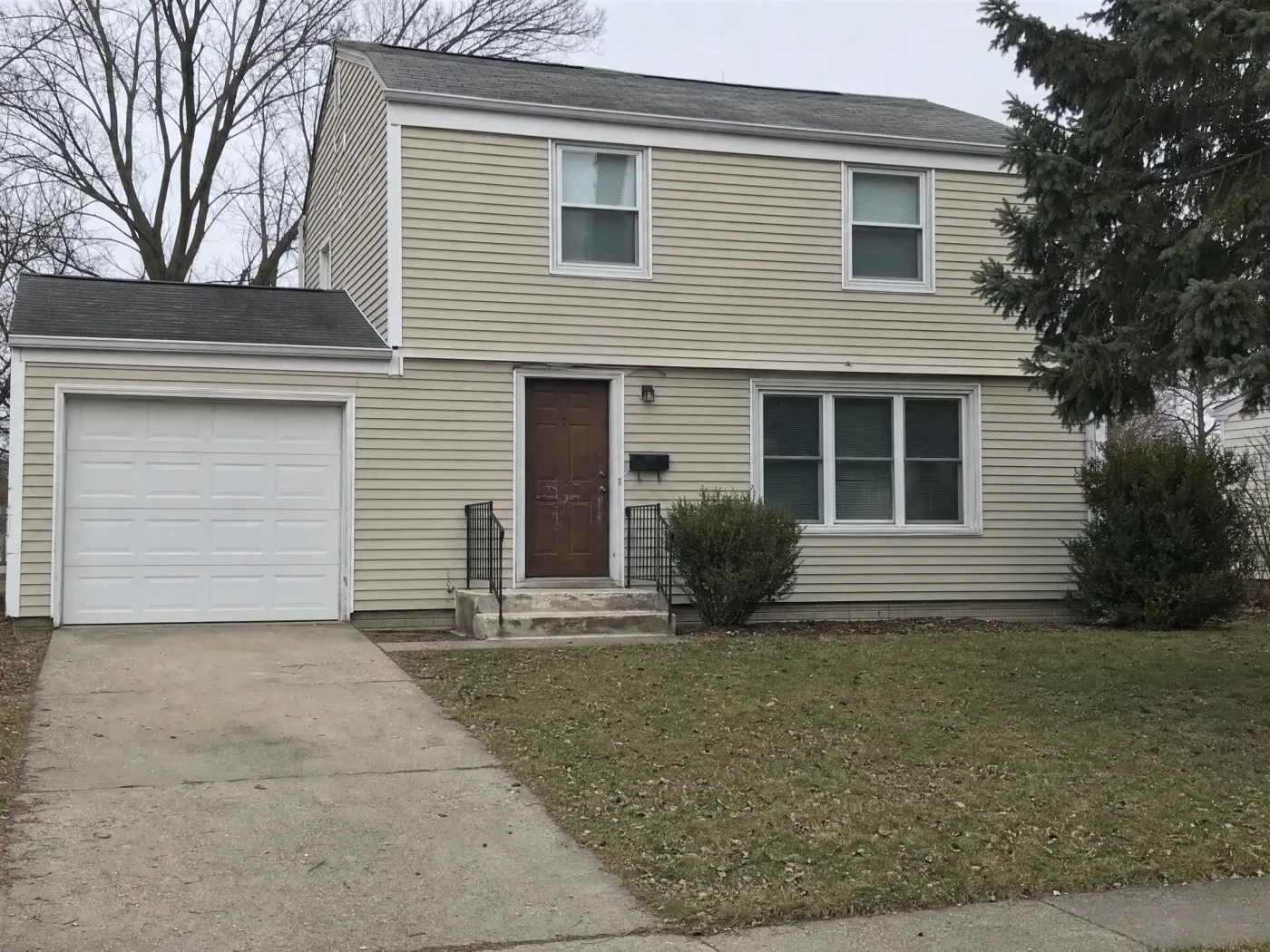 A two-story house with faded beige vinyl siding and a worn brown front door, with four Spot Edit pins on the siding, the front door, the garage door, and the front steps, while the roof, windows, lawn, and spruce tree are left unpinned