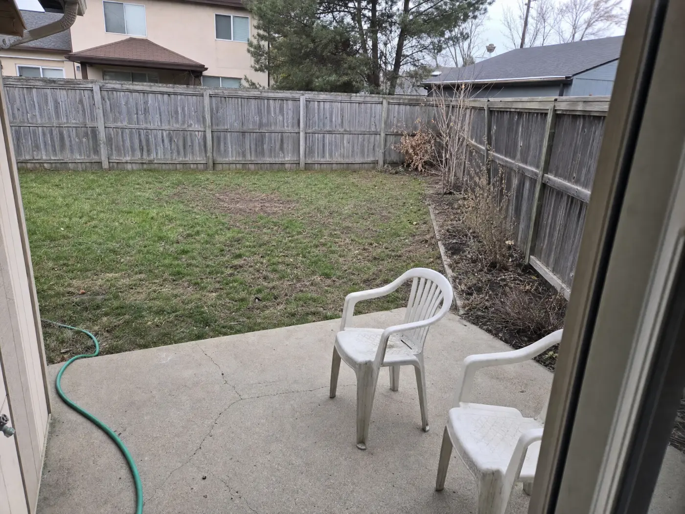 A neglected suburban backyard with patchy lawn, a bare fence, and a small concrete slab before landscape design
