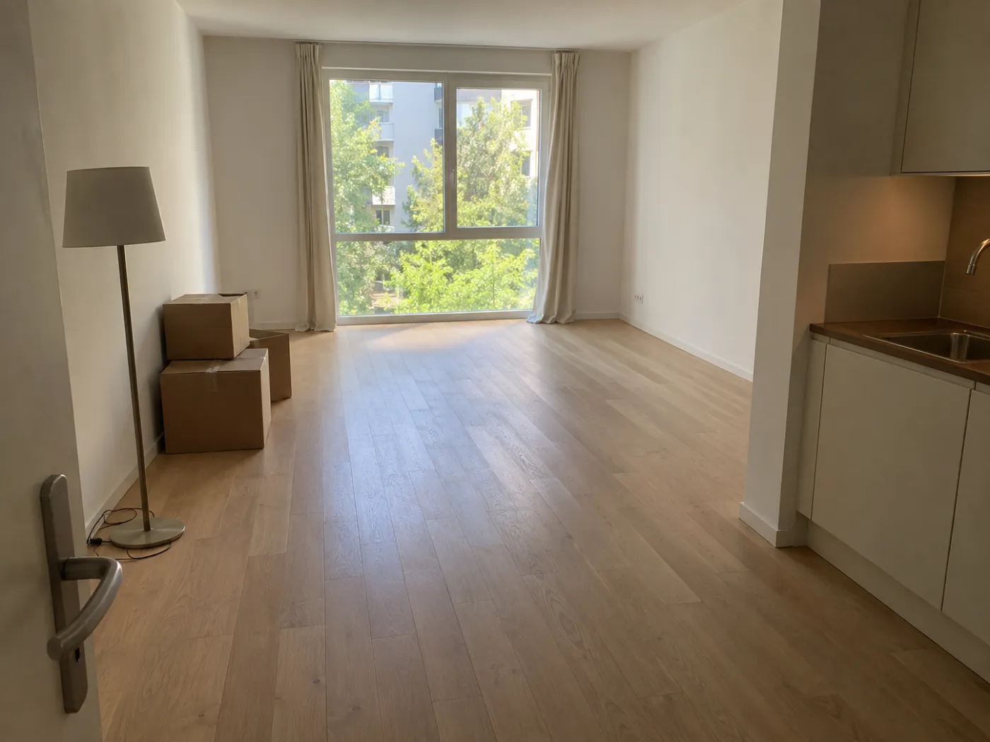 An empty studio apartment right after moving in, with a tall window, a kitchenette on the right, moving boxes, and a floor lamp, the starting point for AI Ideas in Idori